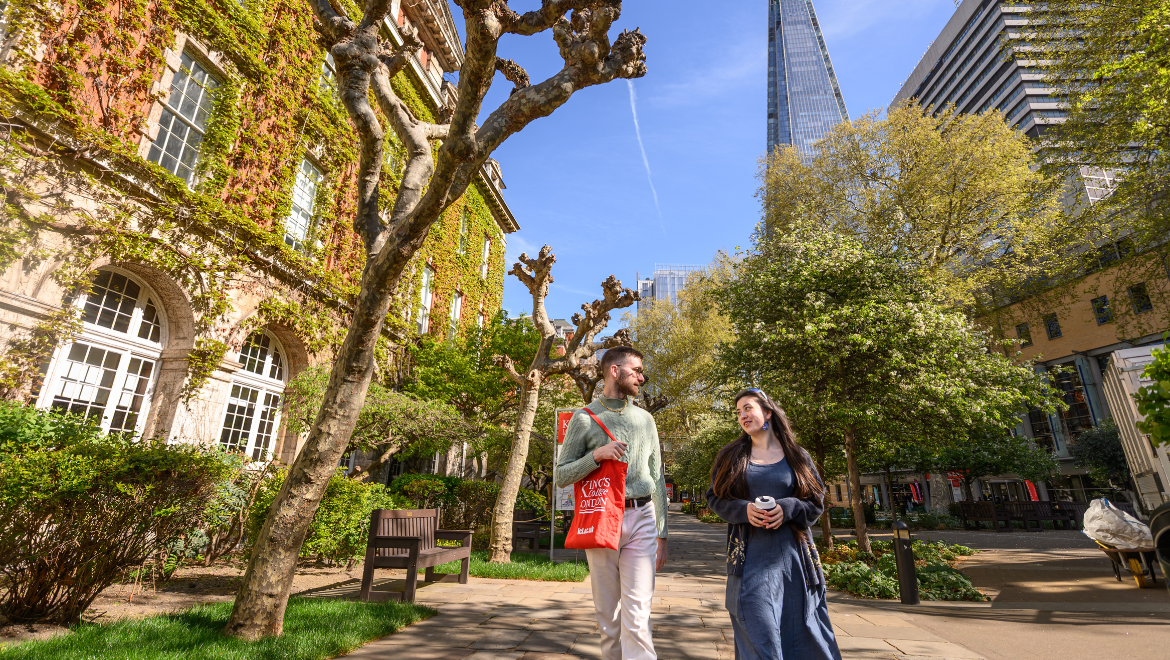 Two students walking across Guy's courtyard with a King's-branded tote bag